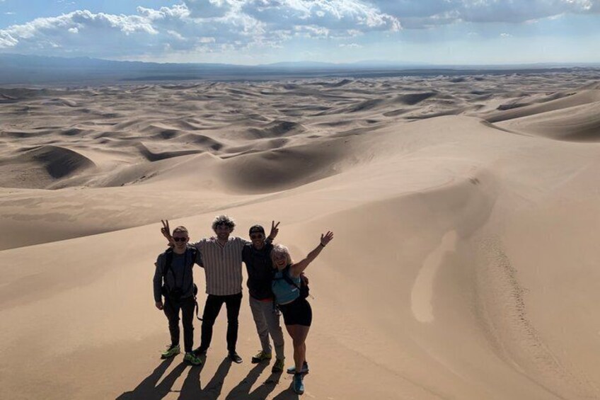 Three people standing on a sand dune with a vast desert landscape in the background. 2