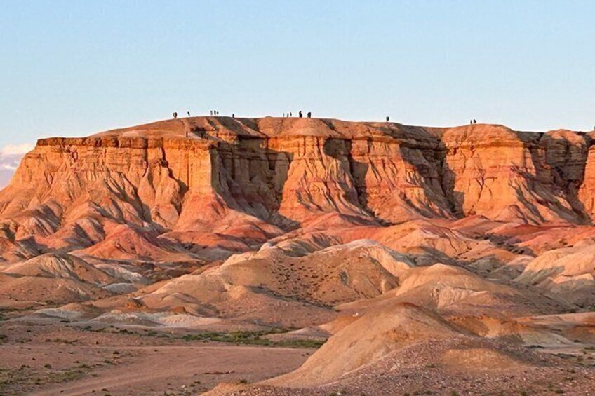 A rugged, layered rock formation with people standing on top. 4