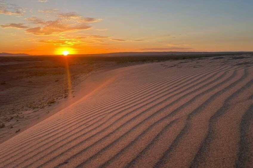 A desert landscape with rippled sand dunes and a setting sun. 3