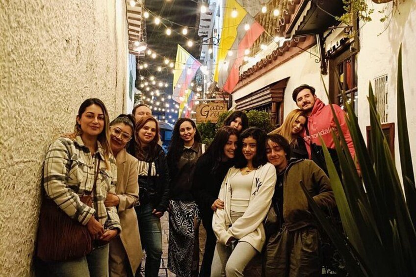 A group of people posing in a narrow street with string lights and a building with a sign. 4