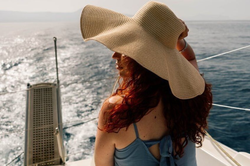 A person with red hair wearing a straw hat and a blue swimsuit, looking out over the ocean from a boat. 5