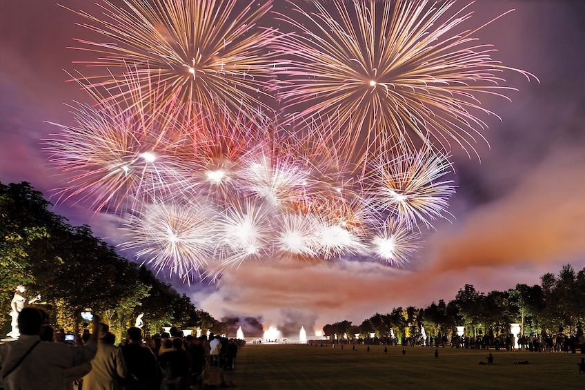 Fuegos artificiales sobre un parque con estatuas y gente. 2