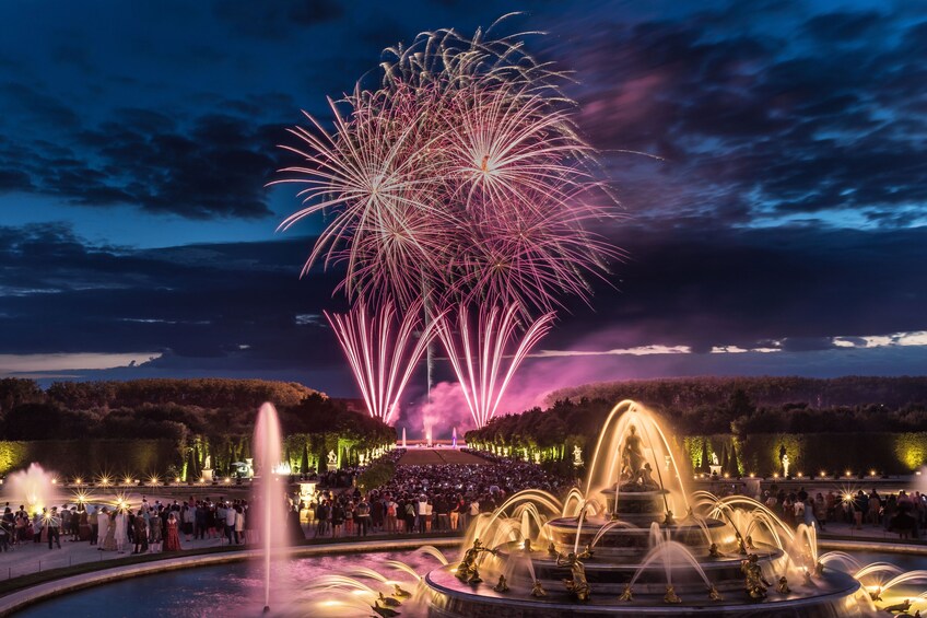Un evento nocturno al aire libre con fuegos artificiales, gente y una fuente. 1