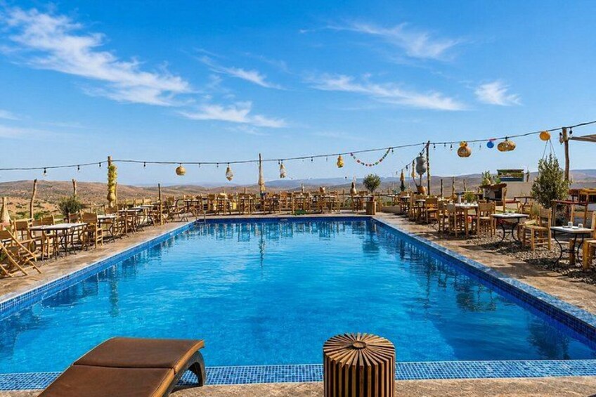 A swimming pool with lounge chairs and tables, surrounded by a desert landscape. 1