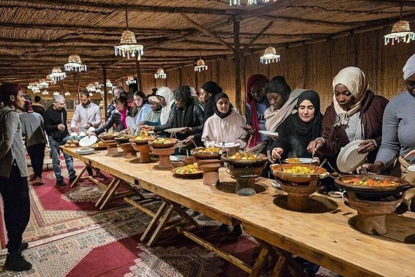 A communal meal with people serving themselves from large pots on a long table in a rustic setting. 2