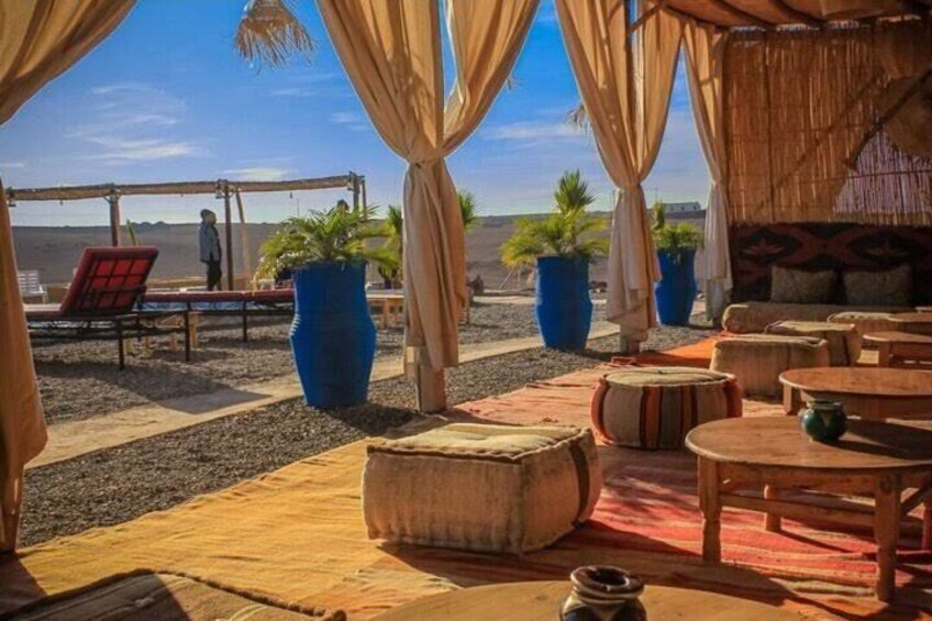 A desert setting with a thatched-roof structure, outdoor seating, and large potted plants. 3