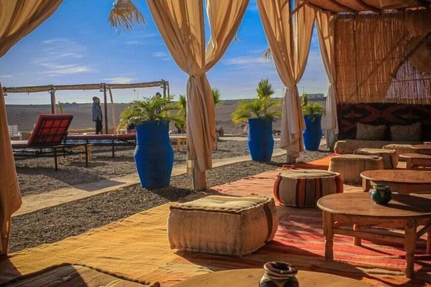 A desert setting with a thatched-roof structure, outdoor seating, and large potted plants. 3