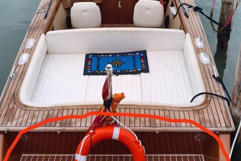 A boat's interior with a white cushioned seating area, a steering wheel, and a life ring. 3