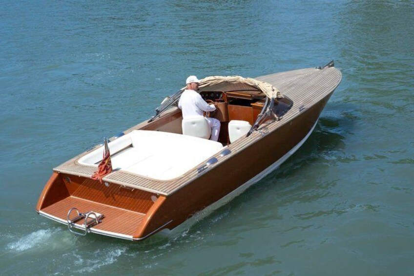 A wooden motorboat with a canopy, a white interior, and a person steering. 5