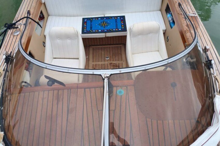 A boat's interior with a steering wheel, control panel, and cushioned seating. 2