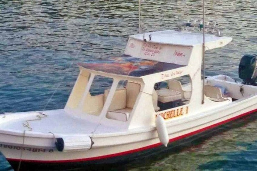 A small white boat with the name 'MICHELLE I' on its side, docked in calm water. 2