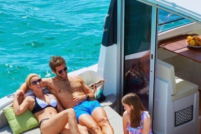A boat with people relaxing on the deck, a cooler, and a bowl of fruit. 2