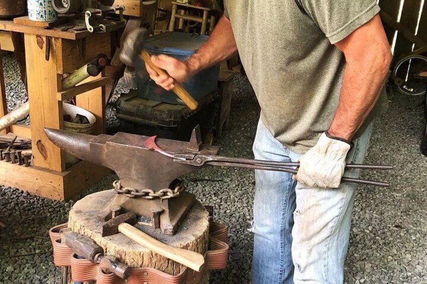 A person working with a hammer and an anvil, surrounded by tools and equipment. 3