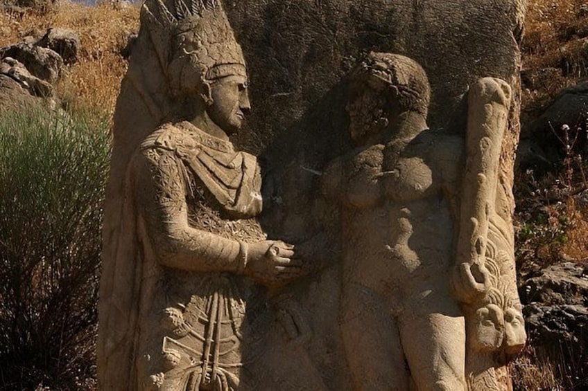 A stone carving of a figure in ancient attire, a rough terrain background, and a clear sky. 2