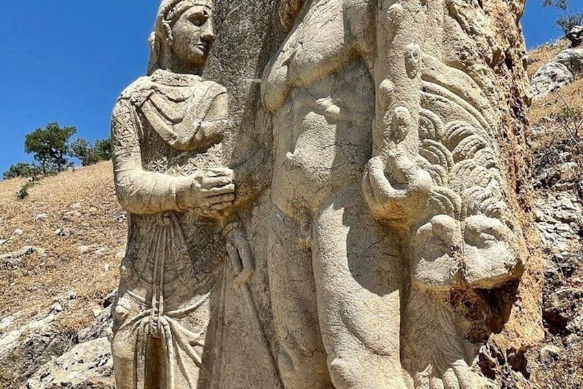 A stone carving of a figure holding a scroll, set against a rocky hillside. 4