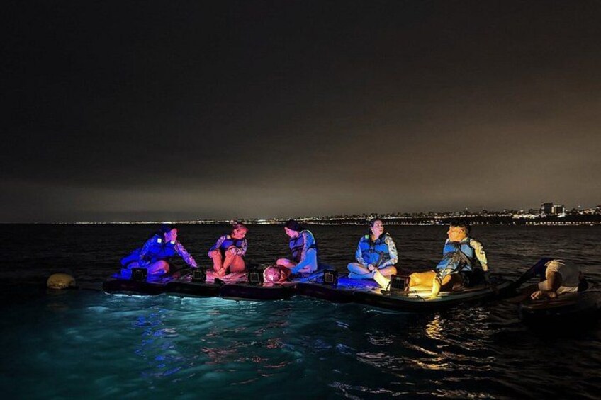 A group of people on a boat at night with city lights in the background. 4