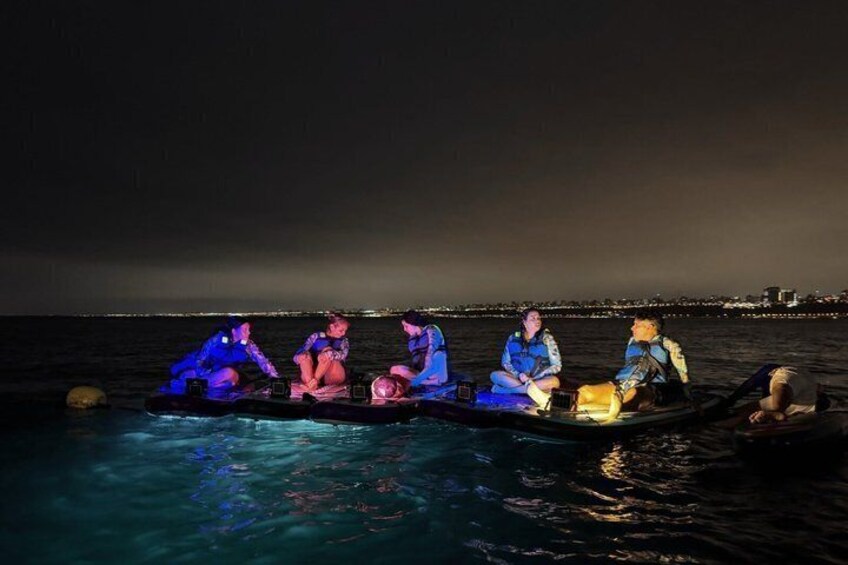 A group of people on a boat at night with city lights in the background. 4