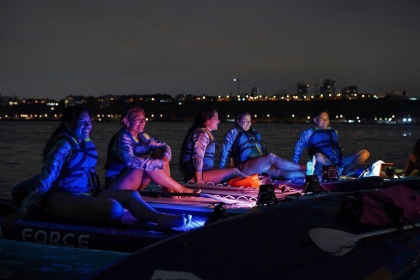 A group of people on a boat at night with city lights in the background. 3