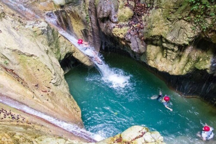 A waterfall in a rocky gorge with two people in the water. 2