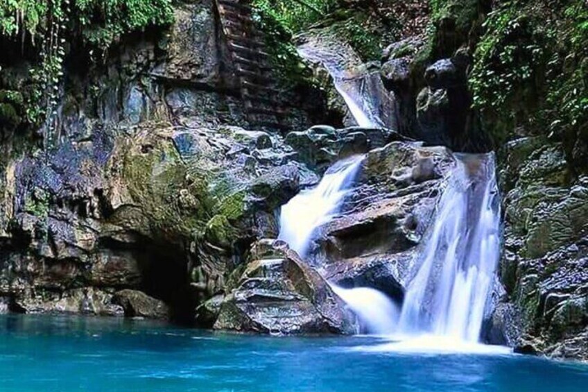 A waterfall cascading over rocks into a clear blue pool surrounded by lush greenery. 4
