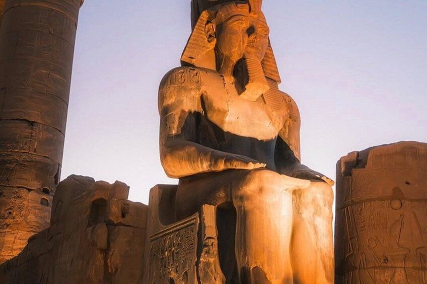 En stor, forntida egyptisk staty med hieroglyfer, placerad framför en bakgrund av stenkolonner och andra byggnadsverk. 2