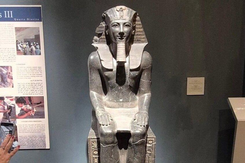 En stor stenskulptur som föreställer en sittande figur med ett huvudstycke, placerad på en piedestal. 5