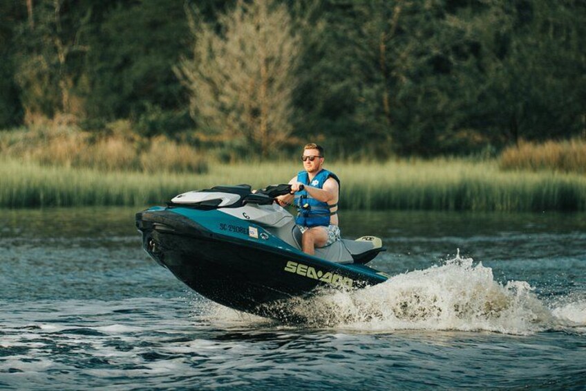 Una persona montando en un jet ski sobre aguas tranquilas, con árboles al fondo. 1