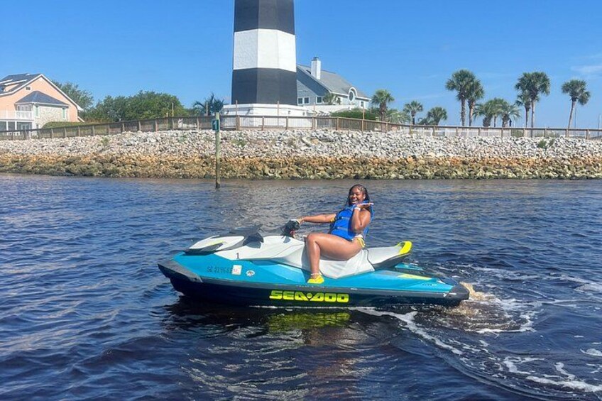 Una persona surfeando en moto acuática sobre un cuerpo de agua, con un faro al fondo. 2