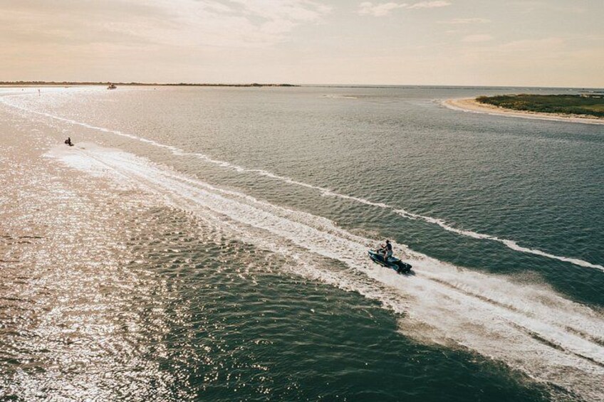 Un jet ski sobre un mar tranquilo, con estela y una costa lejana, bajo un cielo despejado. 5
