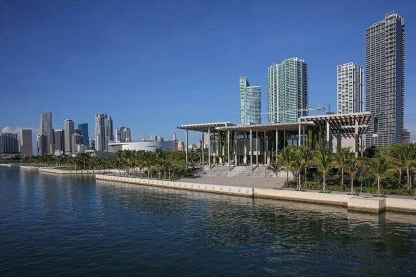 A waterfront cityscape with modern high-rise buildings, a marina, and a covered pedestrian walkway. 1