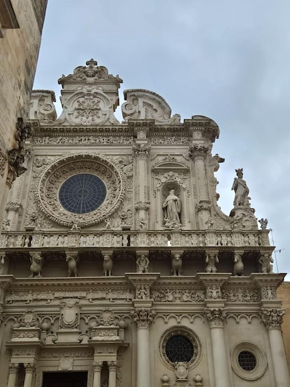 A detailed architectural facade with ornate carvings, a large circular window, and statues. 4