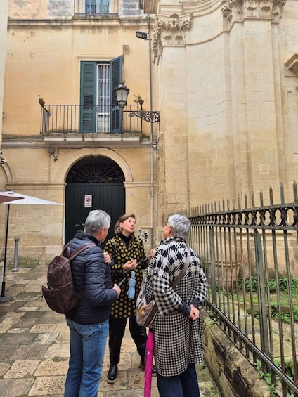 A group of people conversing outside a building with a black door and green shutters. 3