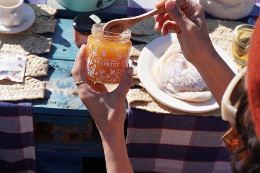 A person holding a jar of honey with a spoon, sitting at a table with a checkered tablecloth. 2