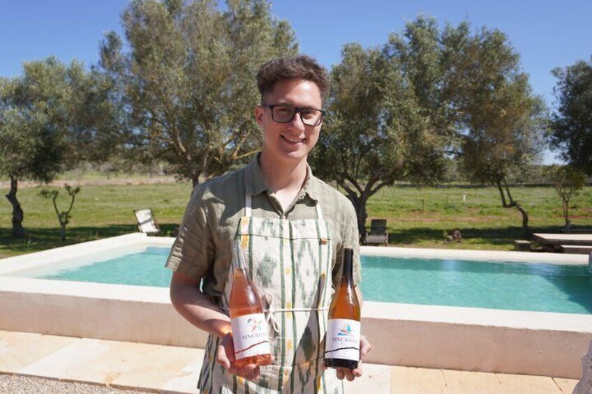 A person holding two bottles of wine in front of a swimming pool with trees in the background. 5