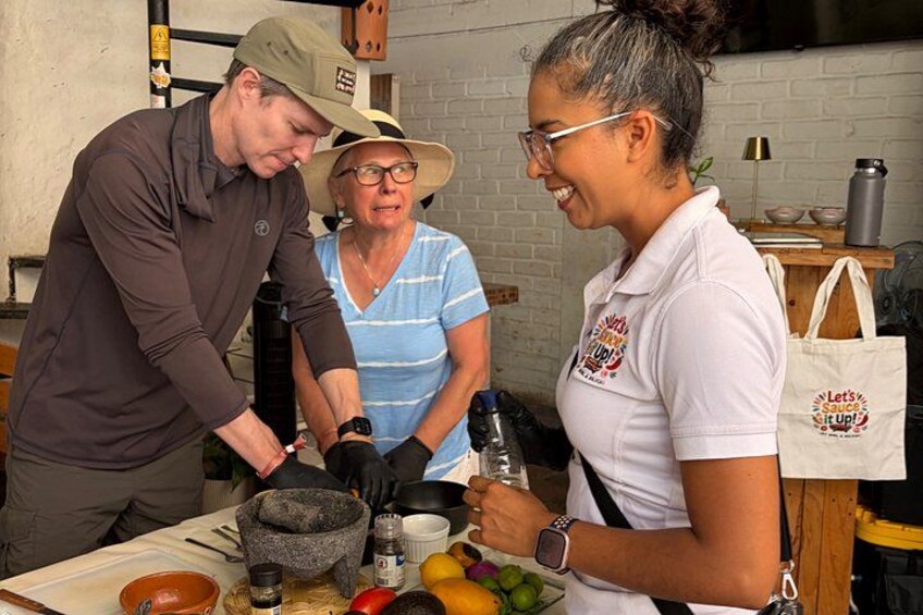 Three people preparing food with a mortar and pestle, a cutting board, and various ingredients. 3