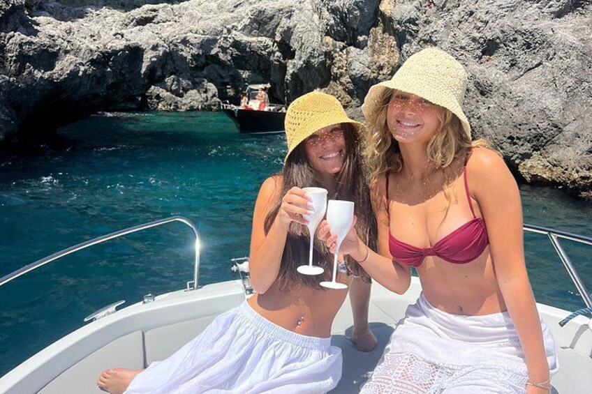 Two people on a boat near rocky cliffs and clear blue water. 1