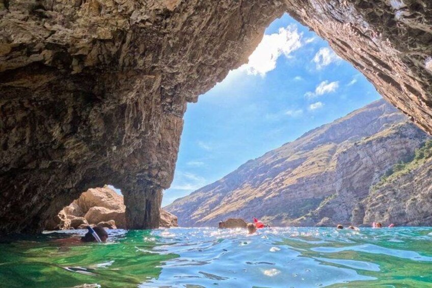 A natural rock formation with a water body and people swimming. 4