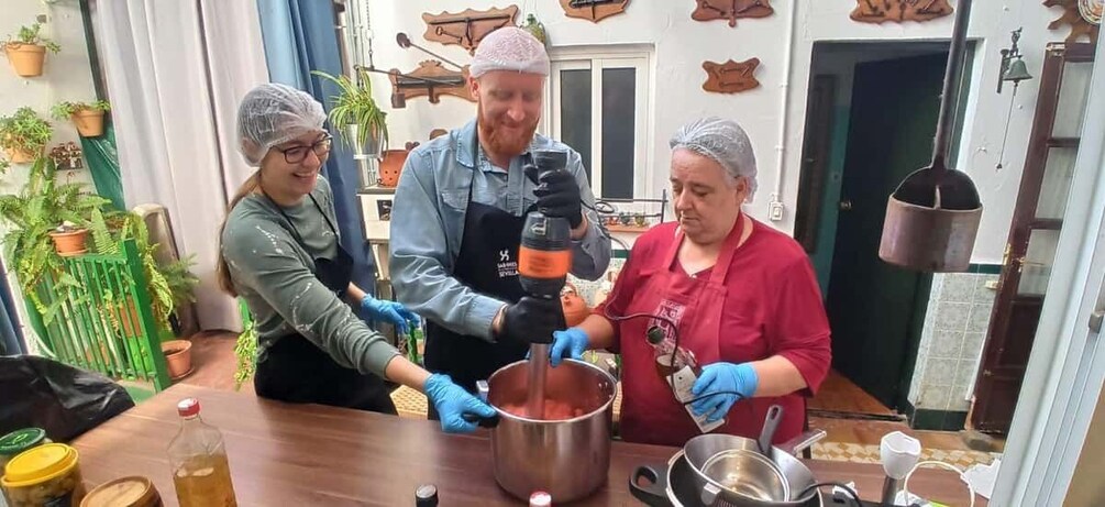 Three people in a kitchen preparing food with a pot on the stove. 1
