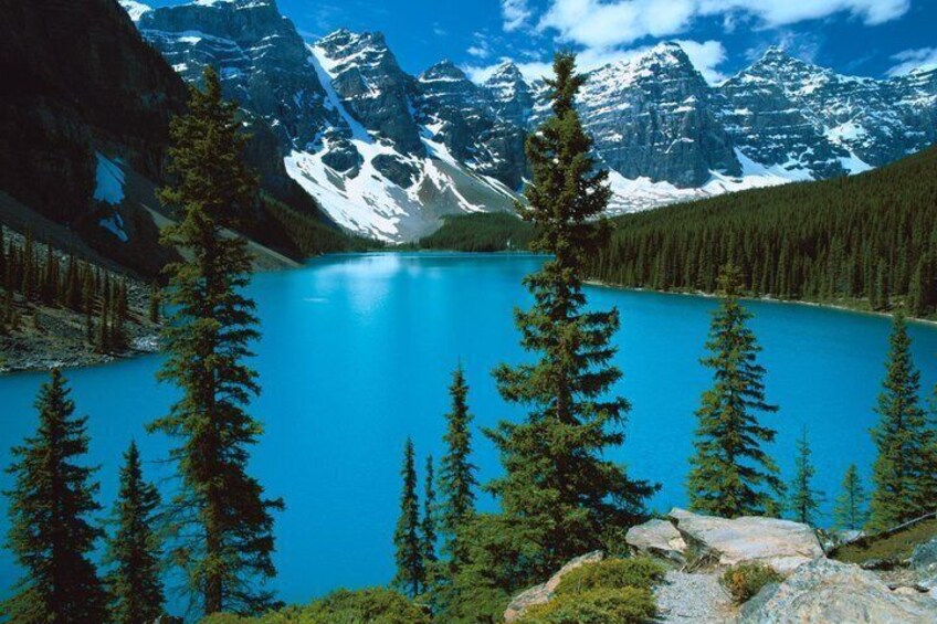 A turquoise lake surrounded by coniferous trees and snow-capped mountains. 1