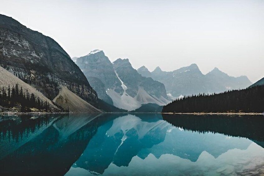 A calm lake reflecting mountains, surrounded by dense forests. 4