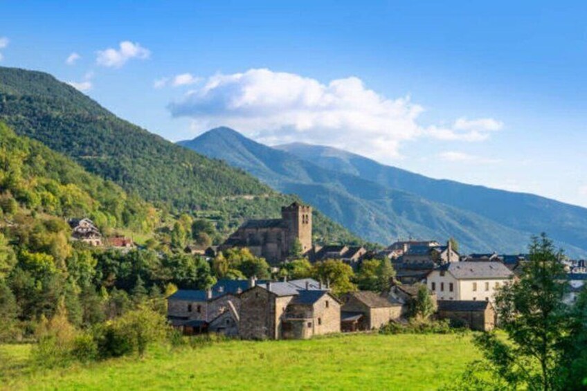 A village with stone buildings, a church tower, and mountains in the background. 2