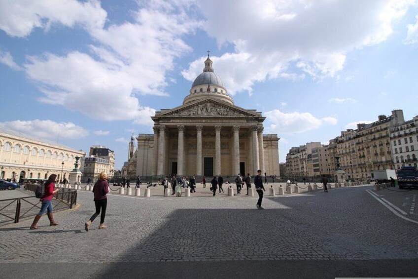 A historic building with columns and a dome, surrounded by a cobblestone square with pedestrians. 3