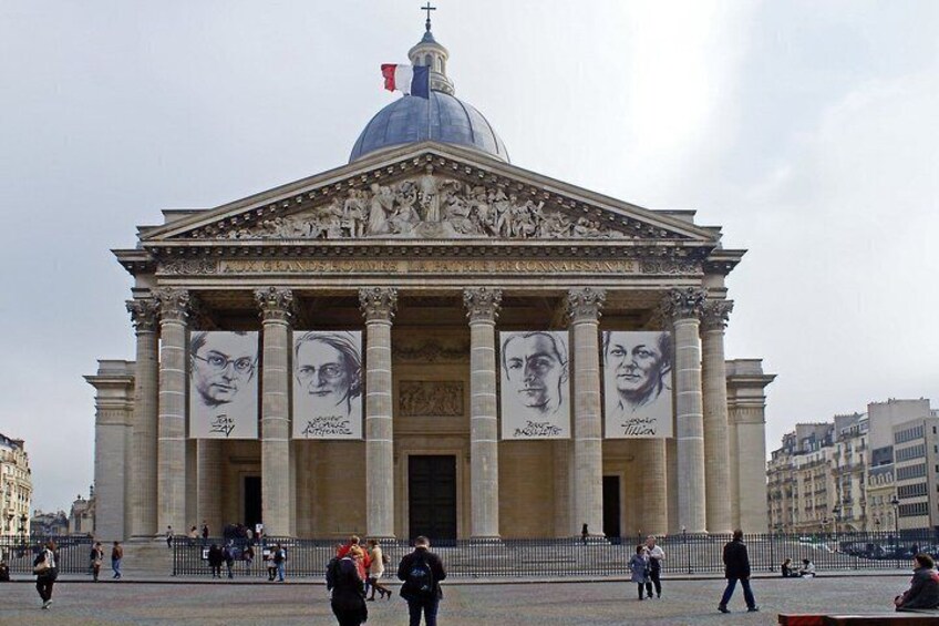 A historic building with a dome and columns, featuring large portraits on its facade. 2