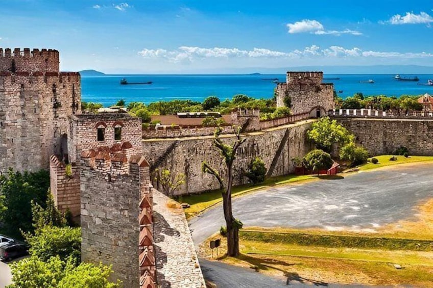 A historic stone fortress with a moat, a clear blue sea, and a few boats in the distance. 4