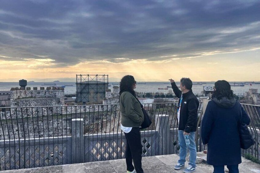 Three people standing on a rooftop overlooking a cityscape with a cloudy sky. 5