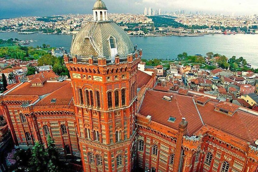 A large red brick building with a dome and a tower, surrounded by a cityscape and a body of water. 5
