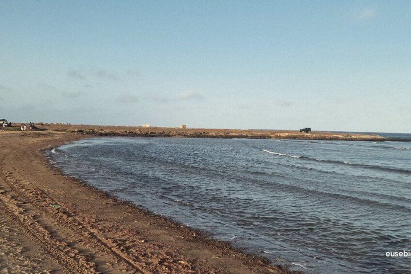A coastal beach with a rocky shoreline, calm sea, and distant buildings. 3