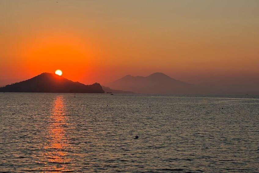 A sunset over a calm sea with a mountain in the background. 1