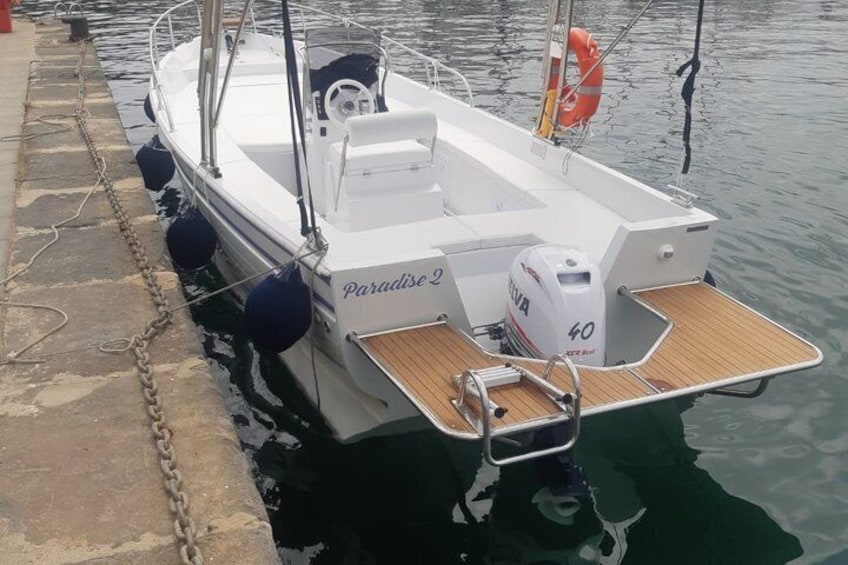 A small white boat named 'Paradise 2' docked at a pier with a wooden deck and a motor. 4