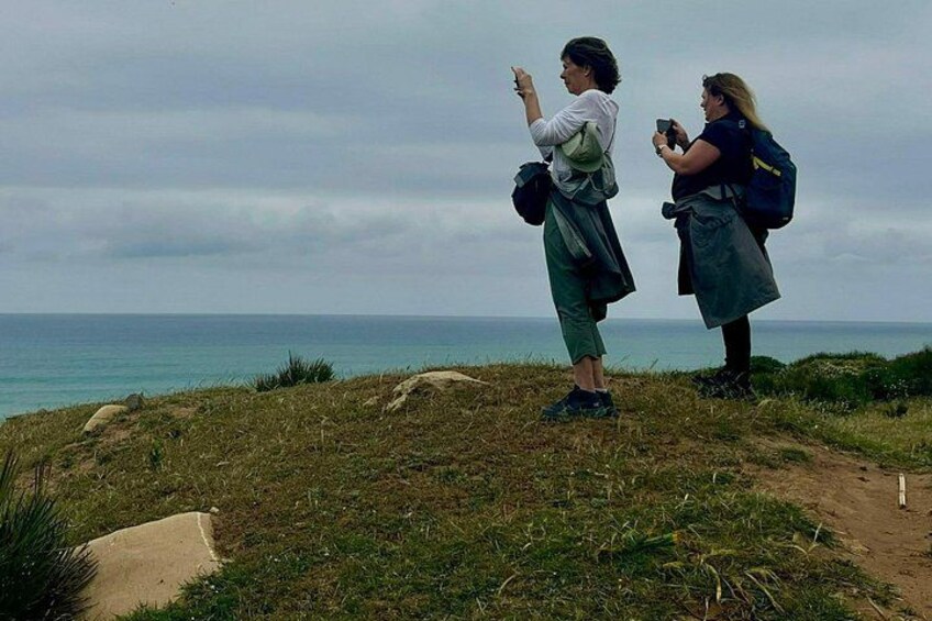 Two people taking photographs on a grassy hill overlooking the sea. 4